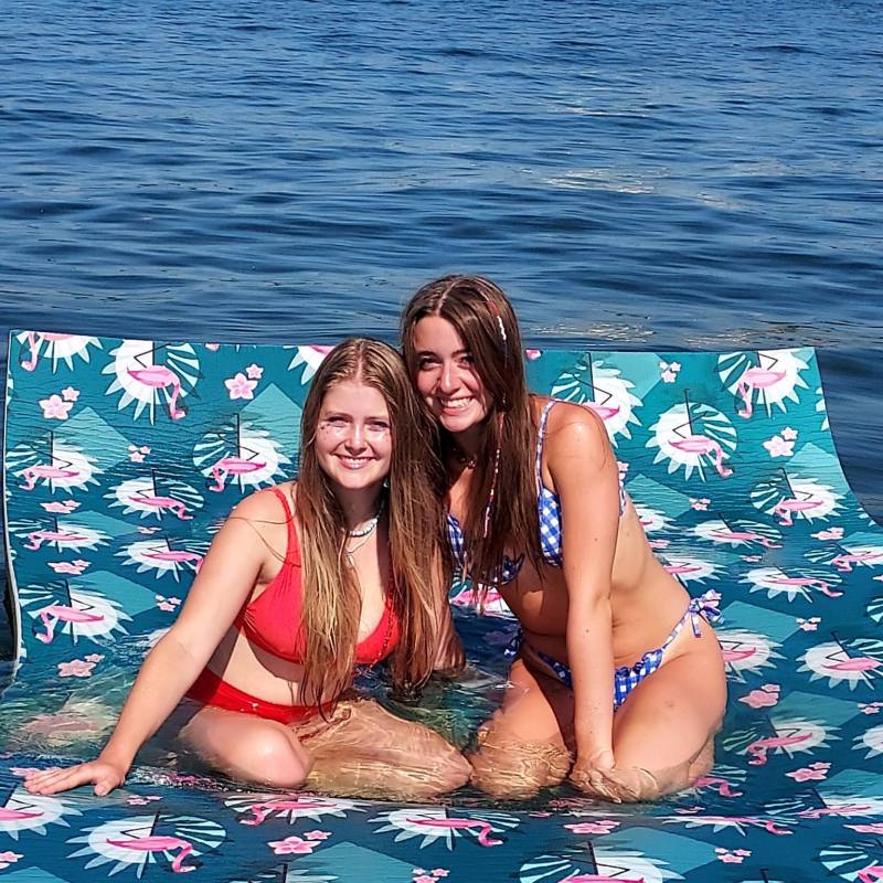 Two women in swimsuits sitting on a floral inflatable in the water.