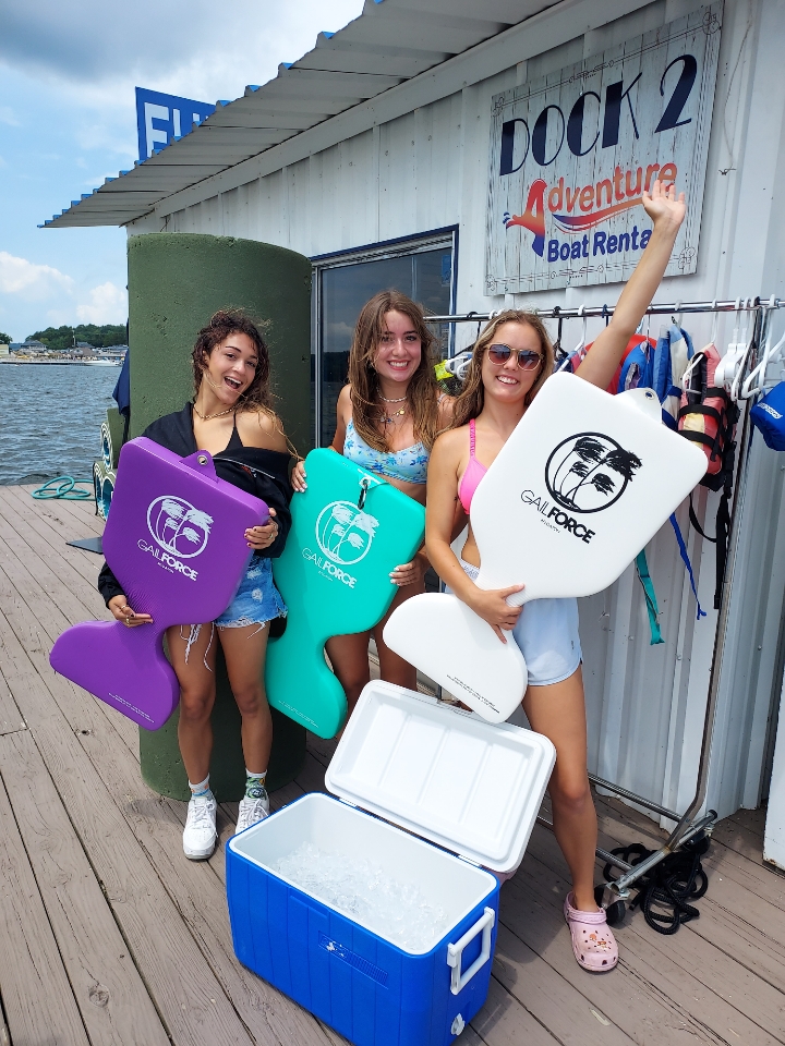 Three people holding colorful swimming boards next to a cooler on a dock.
