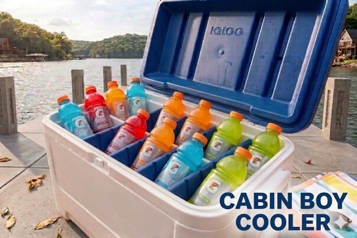 Open cooler with colorful sports drinks by a lakeside.