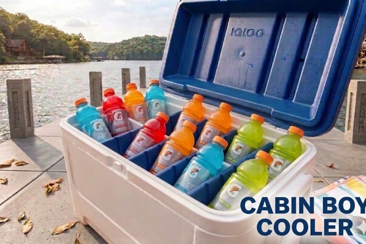 Open cooler with colorful sports drinks by a lakeside.