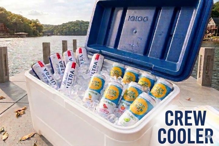 Cooler with assorted drinks by a lake.