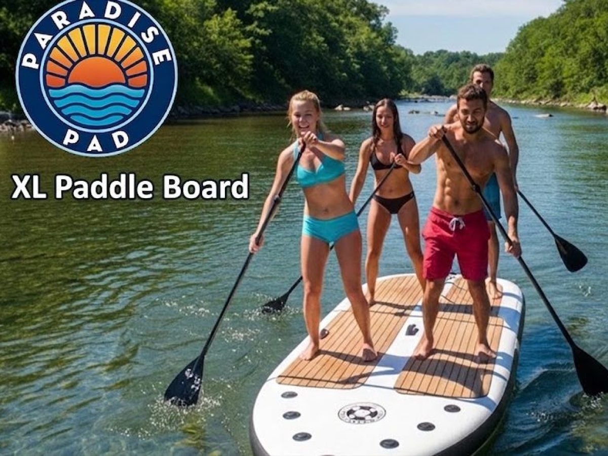 Four people paddle boarding on a large board in a river, surrounded by greenery.