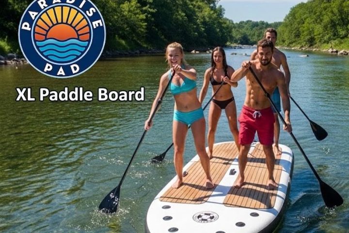 Four people paddle boarding on a large board in a river, surrounded by greenery.