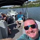 People on a party boat ride on a sunny day, with one person taking a selfie.